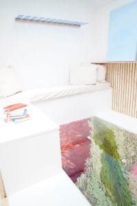 Shed detail: Ledge seat, white throw pillows, and colorful floor.