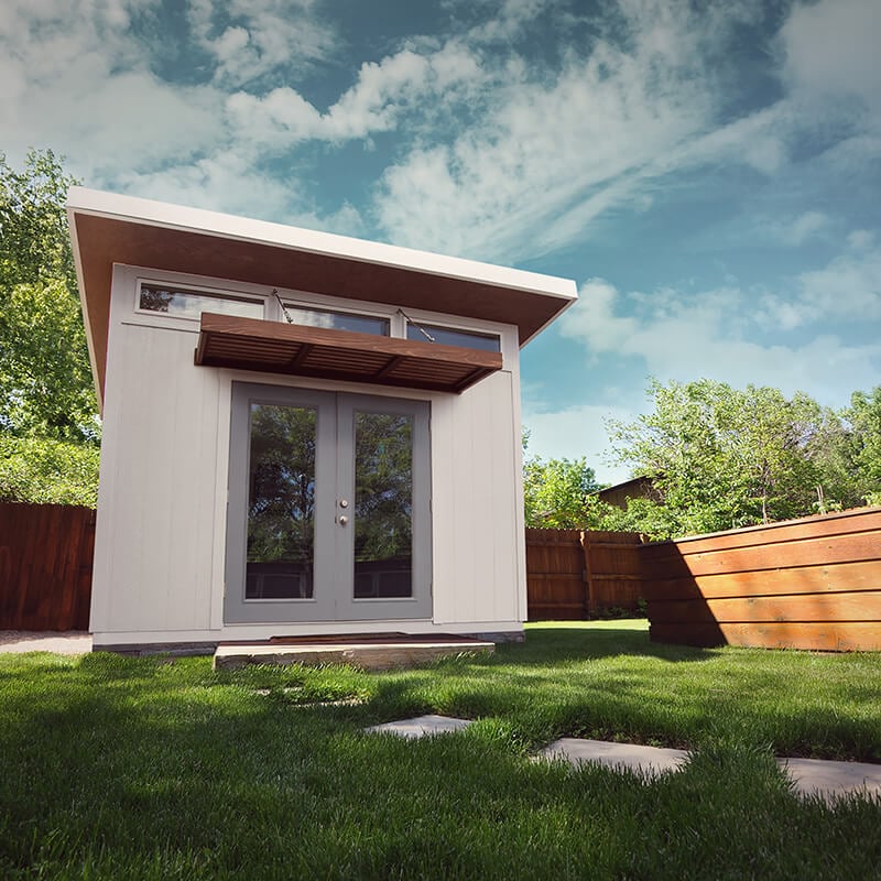White studio style shed in back yard under cloudy sky.